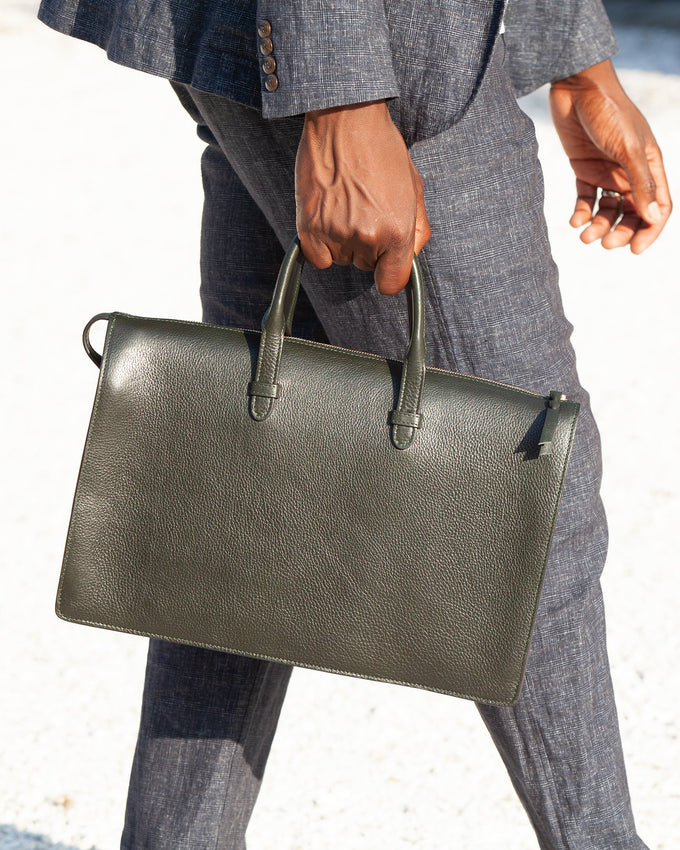 Person holding a green leather briefcase against a light background